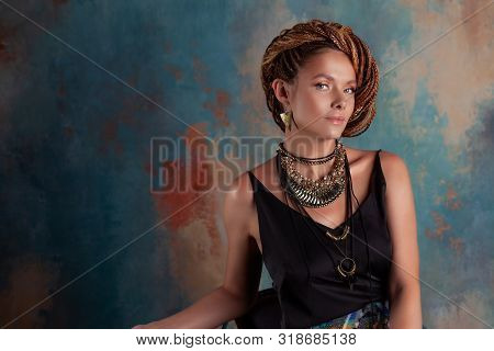 Southern Spices. A Beautiful Young Blue-eyed Woman With Afrocos And Large Ornaments Against A Textur