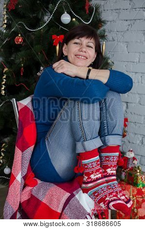 Older Adult Beautiful Brunette Woman In Casual Sitting In A Chair In Christmas Decorations Under The