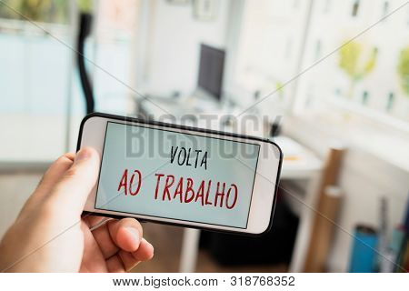 closeup of a man at the office with a smartphone in his hand with the text volta ao trabalho, back to work written in portuguese, in its screen