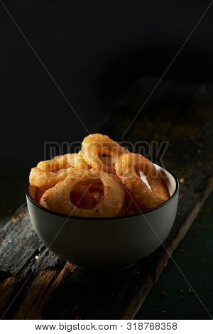 closeup of a white ceramic bowl with some calamares a la romana, fried battered squid rings typical of spain, on a dark rustic wooden table against a black background with some blank space on top