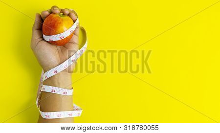 Close Up Of The Red Apple On The Left Hand Wrapped Around A Tape Measure, Health And Dieting Concept