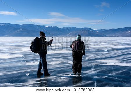 Russia, Sarma - Febrary 24, 2019: Man Takes Photo With Phone And Woman Wallks On Frozen Lake Baikal 