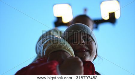 Smiling Young Mother And Happy Daughter Under Street Lantern On Evenig Sky Background. Bottom View.