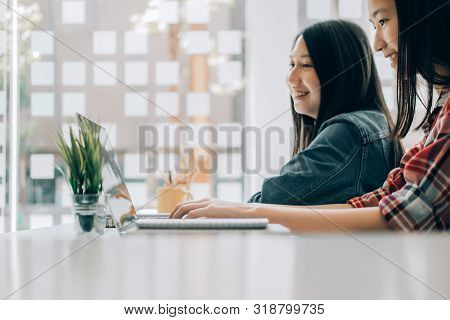 Young Studebt Sitting At Table In Library College Writing And Working On Notebook With Laptop, Educa
