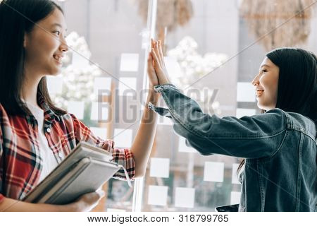 Young Studebt Sitting In Library Studying Sharing Knowledg And Giving High-five While Their Colleagu