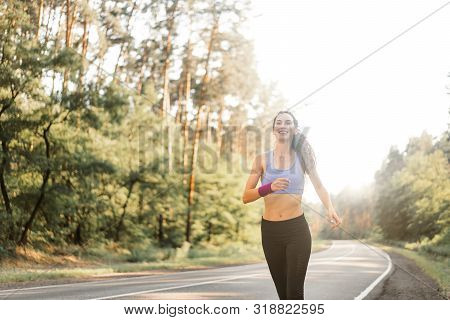 Beautiful Caucasian Young Girl Athlete Runs Sunny Summer Day On Asphalt Road In The Pine Forest. Wom