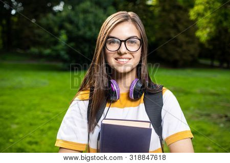 Portrait Of Smiling Student Girl With Daypack And Books In Park