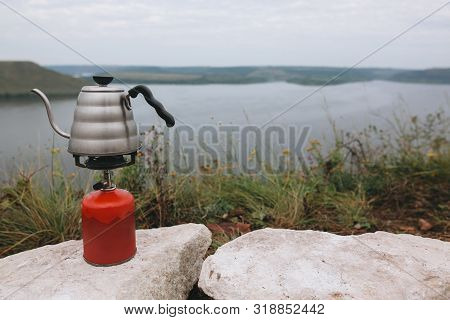 Steel Kettle Boiling On Gas Primus, Making Hot Drink At Picnic Outdoors. Brewing Coffee In The Morni