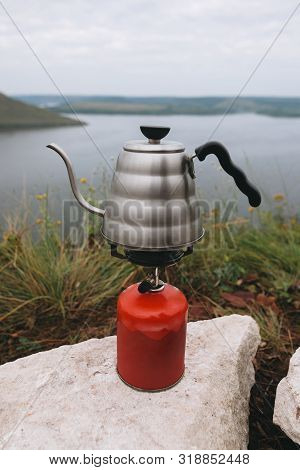 Brewing Coffee In The Morning While Camping On Cliff On Background Of Lake. Steel Kettle Boiling On 