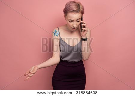 A Girl With Short Pink Hair And A Tattoo In A Gray Top Involuntarily Speaks On The Phone While Stand