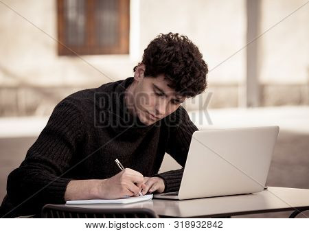 Handsome Young Man Working On Laptop Computer Outside Terrace In An European City Coffee Shop. Stude