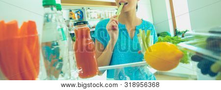 Portrait of female standing near open fridge full of healthy food, vegetables and fruits. Portrait of female