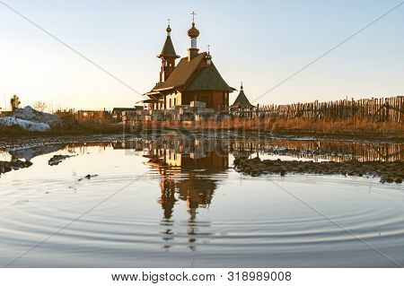 Reflected In A Large Puddle Of Wooden Church Against The Sunset In A Puddle Of Waves In Circles. Woo