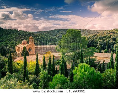 View Of The Fontfroide Abbey (wine-clad Monastery) Surrounded By Trees And Mountains With A Sky Full