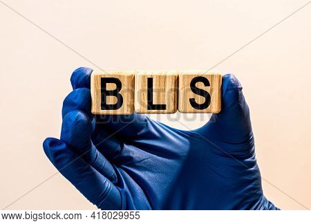 The Word Bls Which Is Made From Wooden Cubes. Hands In A Blue Glove. Isolated On White Background