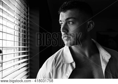 Portrait Of Handsome Man With Beard Standing Next To Window With Open Shirt