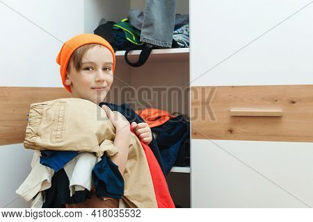 Boy Standing Near Messy Clothes On Shelf. Preteen Boy With Dirty Clothing In His Room. Messy Home Ki