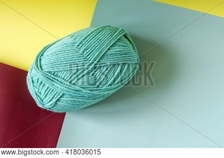 A Ball Of Green Yarn On A Colored Yellow-green-maroon Background Close-up Knitting In Self-isolation