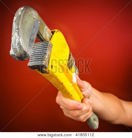 Hand met een monkey wrench op een heldere rode achtergrond