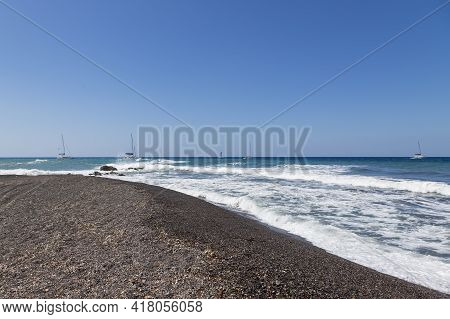Coast And Beach Of Vlychada On Santorini Island In Greece. In The Background Blue Sky And Waves At S
