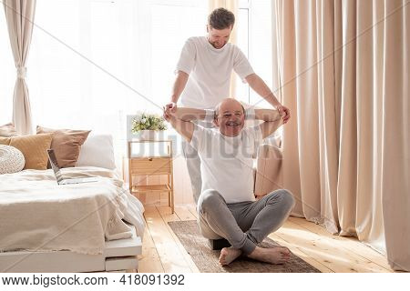 Male Yoga Trainer Helps To Senior Man To Do Asana Correctly.