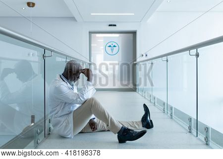 African american male doctor sitting in hospital corridor taking rest and ruminating. medicine, health and healthcare services.