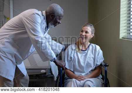 Diverse male doctor and female patient sitting on wheelchair smiling to each other. medicine, health and healthcare services.