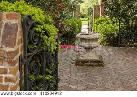 A Small Garden With Trimmed Shrubs, Beautiful Flowering Plants And Trees And A Stone Decorative Bird