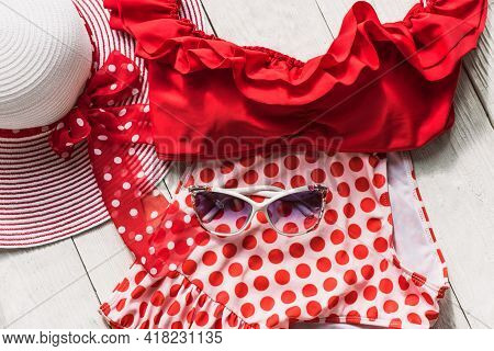 Feminine Red Retro Swimsuit, Hat And Beach Accessories On White Wooden Background. Flat Lay, Top Vie