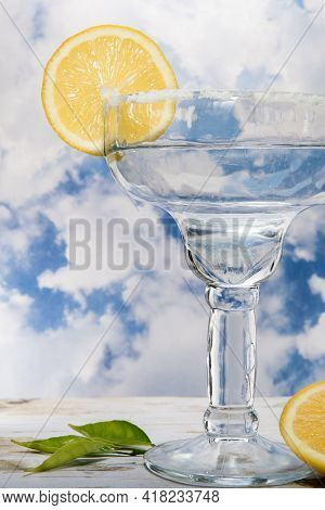Coupe Cocktail Glass With A Lemon Wagon Wheel Garnish And Sugar Rim Against Cloudy Sky.