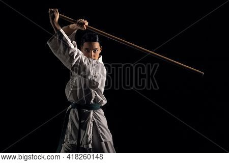 Young Woman In Kimono Practicing With Jodo On A Black Background