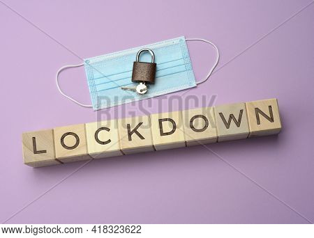 Disposable Medical Mask And And Wooden Blocks With The Inscription Lockdown On A Purple Background. 