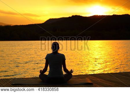 Back View Silhouette Of A Woman Doing Yoga Exercise At Sunset In A Lake Pier