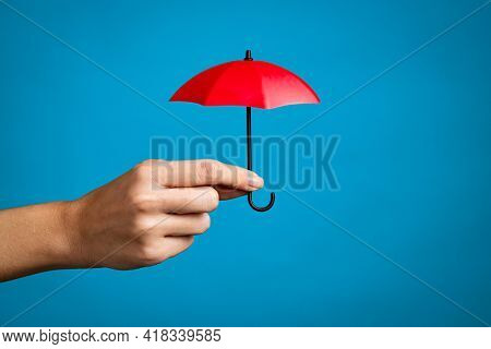 Female hand with small red umbrella isolated on blue background. Close up of woman hand holding mini umbrella against blue wall with copy space. Insurance, protection and security concept.