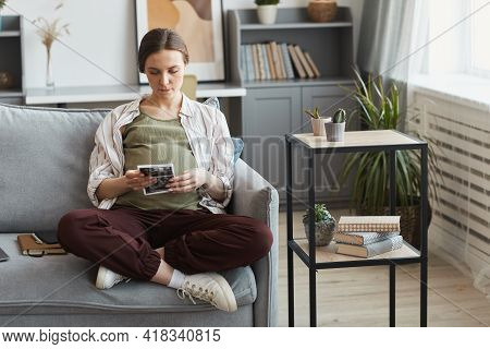 Pregnant Woman Sitting On The Sofa And Examining The Ultrasound Image In The Room