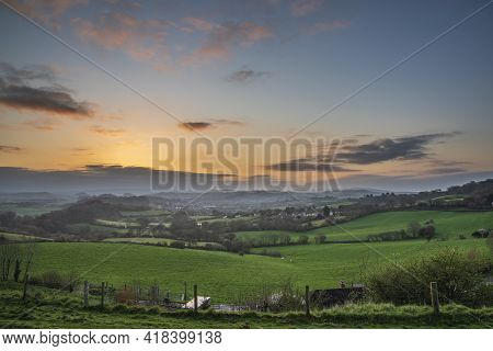 Beautiful Vibrant Sunrise Landscape Image Of Misty View Towards Symondsbury Village In Dorset On A S