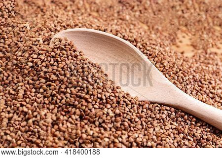 Scattered Buckwheat. Buckwheat In A Wooden Bowl And Spoon Lies On A Wooden Table. Scattered Buckwhea