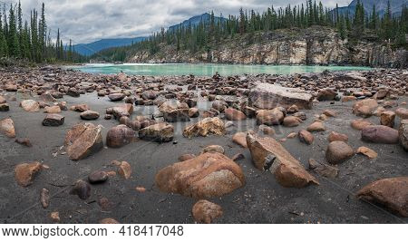 Low Angle Shot Of Sand, Orange Stones And Cliffs In The Banks Of Aqua-colored Glacier Athabasca Rive