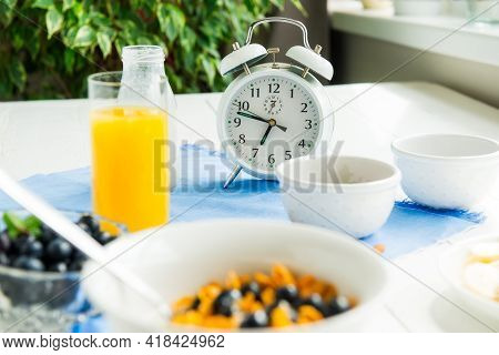 Time For Breakfast. Alarm Clock With Healthy Food. Bowl With Cereals, Nuts And Berries, Milk, Fresh 