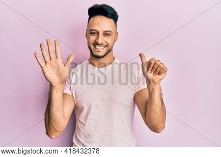 Young arab man wearing casual clothes showing and pointing up with fingers number six while smiling confident and happy. 