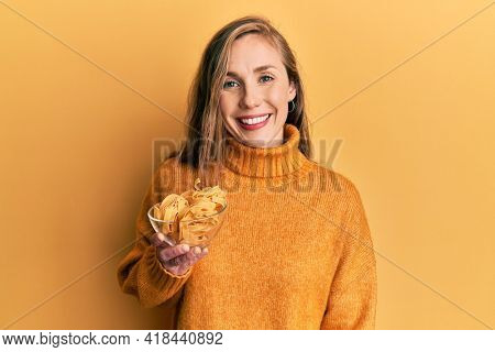 Young blonde woman holding bowl with uncooked pasta looking positive and happy standing and smiling with a confident smile showing teeth 