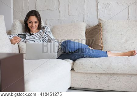 Happy Natural Brunette Using Credit Card And Laptop In The Living Room.