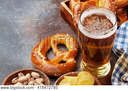 Lager beer mug, nuts, potato chips and fresh baked homemade pretzel with sea salt on stone table. Classic beer snack. With copy space