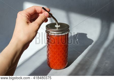 Female Hand Holding Glass Of Tomato Smoothie. Tomato Juice With Pulp On Trendy Minimal Grey Backgrou