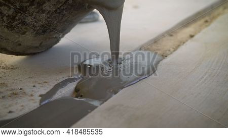 The Solution Is Poured Into The Gap In The Floor. Dark Bucket. Floor Leveling Solution. A Bucket Fro
