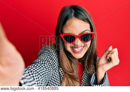 Young brunette woman taking a selfie photo wearing sunglasses screaming proud, celebrating victory and success very excited with raised arm 