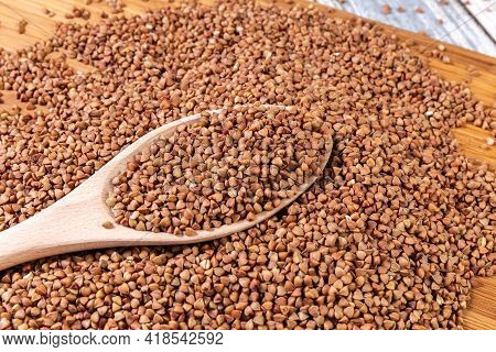 Scattered Buckwheat. Buckwheat In A Wooden Bowl And Spoon Lies On A Wooden Table. Scattered Buckwhea