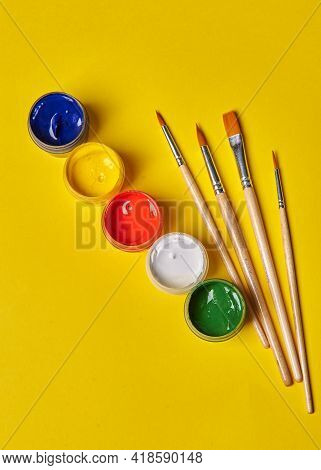 Four Tassels And Colored Gouache Stands On A Yellow Background