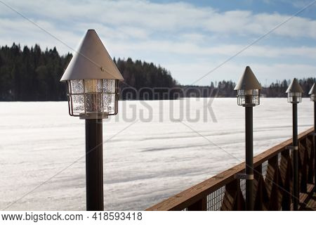 Lanterns Atteched To A Wooden Pier By A Frozen Lake. The Weather Is Quite Nice On This Spring Day.