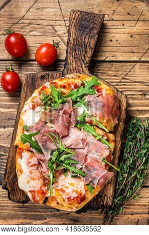 Sliced Pizza With Prosciutto Parma Ham, Arugula And Parmesan Cheese On A Wooden Board. Wooden Backgr